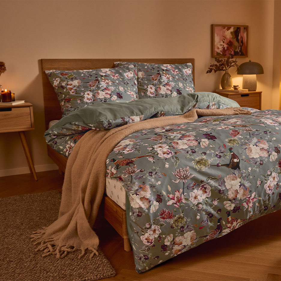 Drveni krevet sa zelenom cvjetnom posteljinom i smeđim pokrivačem.