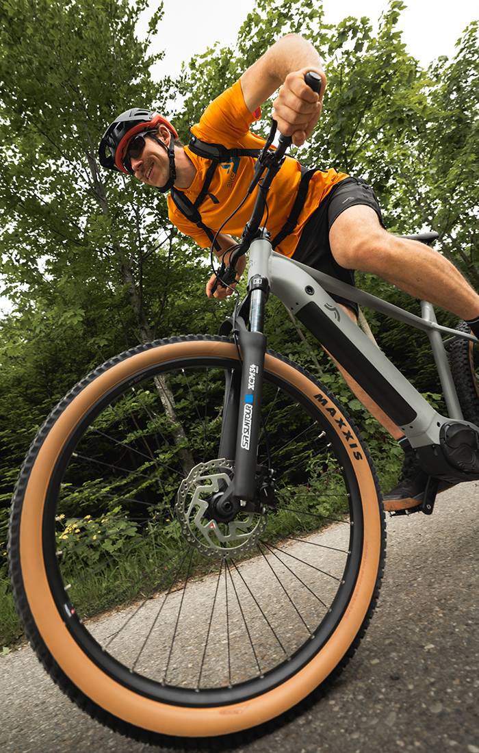 Muškarac vozi sivu električnu biciklu Maxxis kroz šumu.