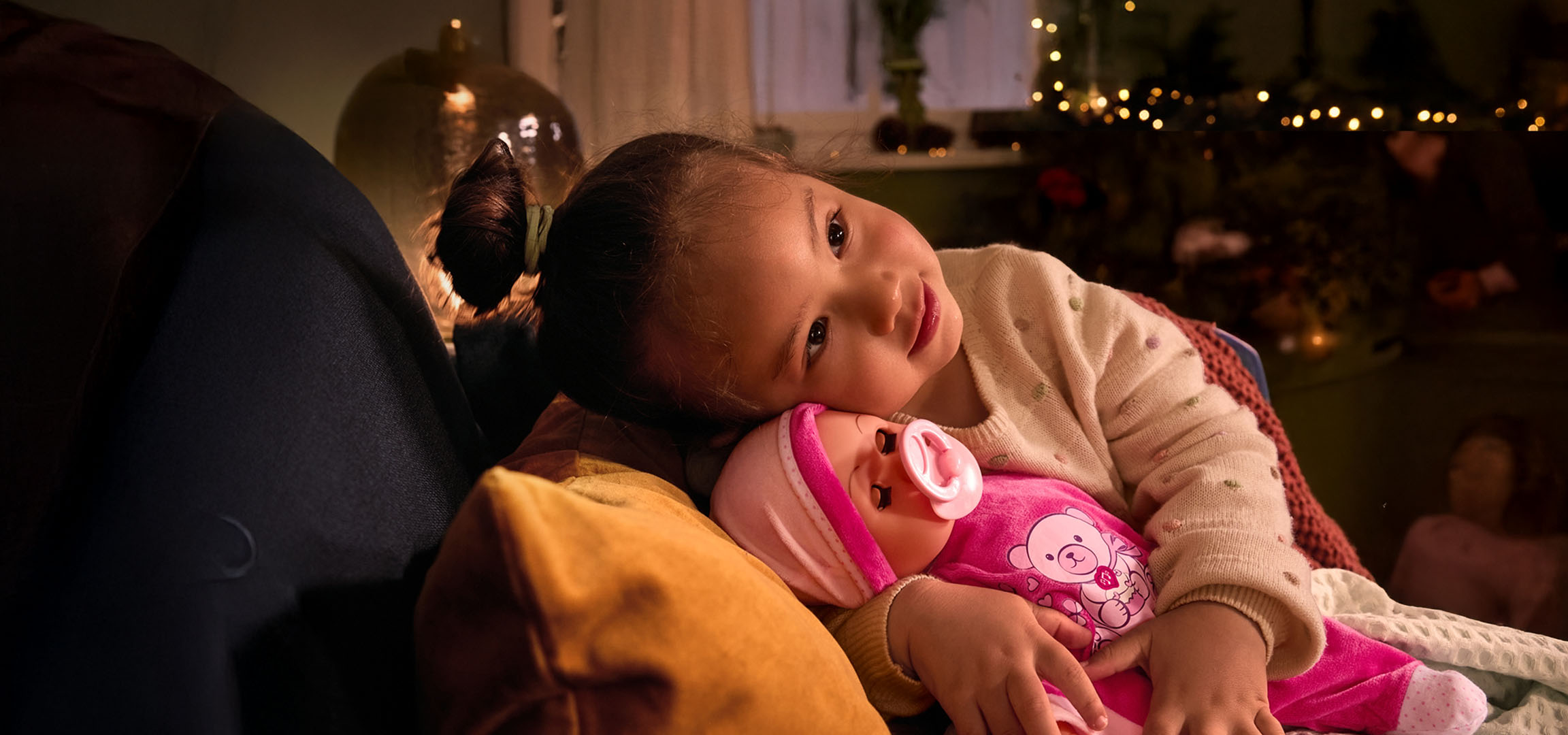 Djevojčica s lutkom i dudom, udobno smještena na jastuku.