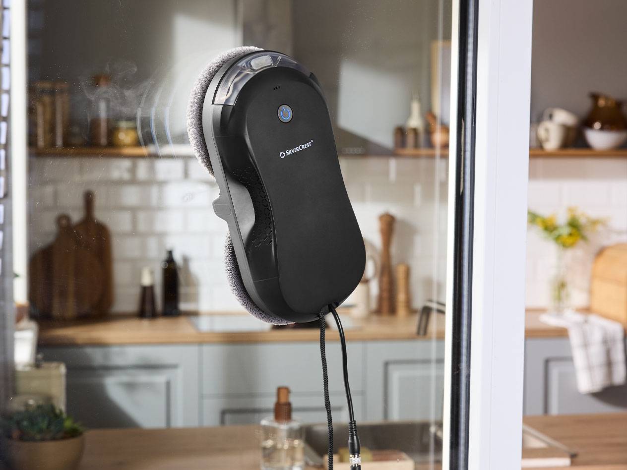 Silvercrest robot za čišćenje prozora na prozorskom staklu s kuhinjom u pozadini.