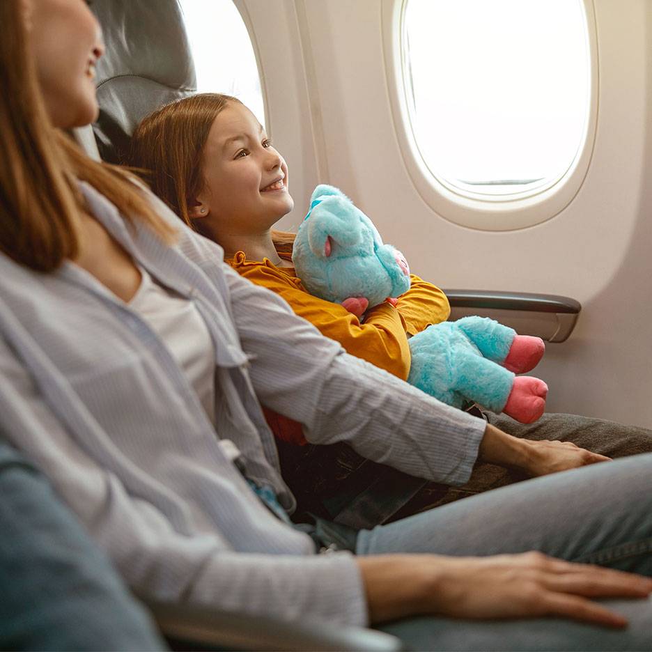 Dijete s plišanom igračkom gleda kroz prozor aviona pored odrasle osobe.