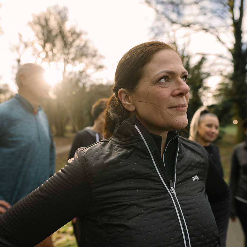 Žena u crnoj sportskoj jakni gleda gore, s grupom ljudi u pozadini.