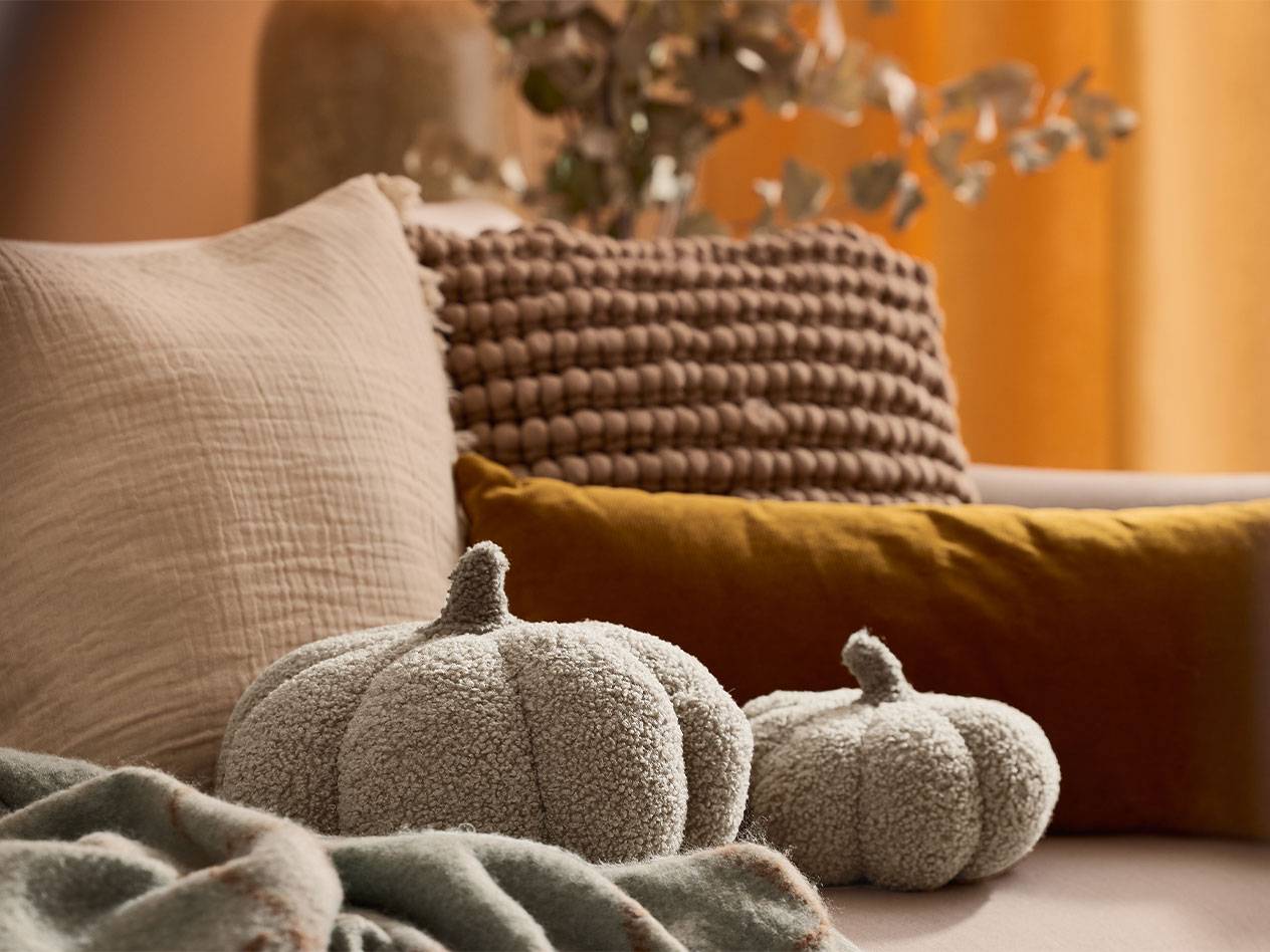Dvije plišane ukrasne bundeve i jastuci u zemljanim tonovima na kauču.
