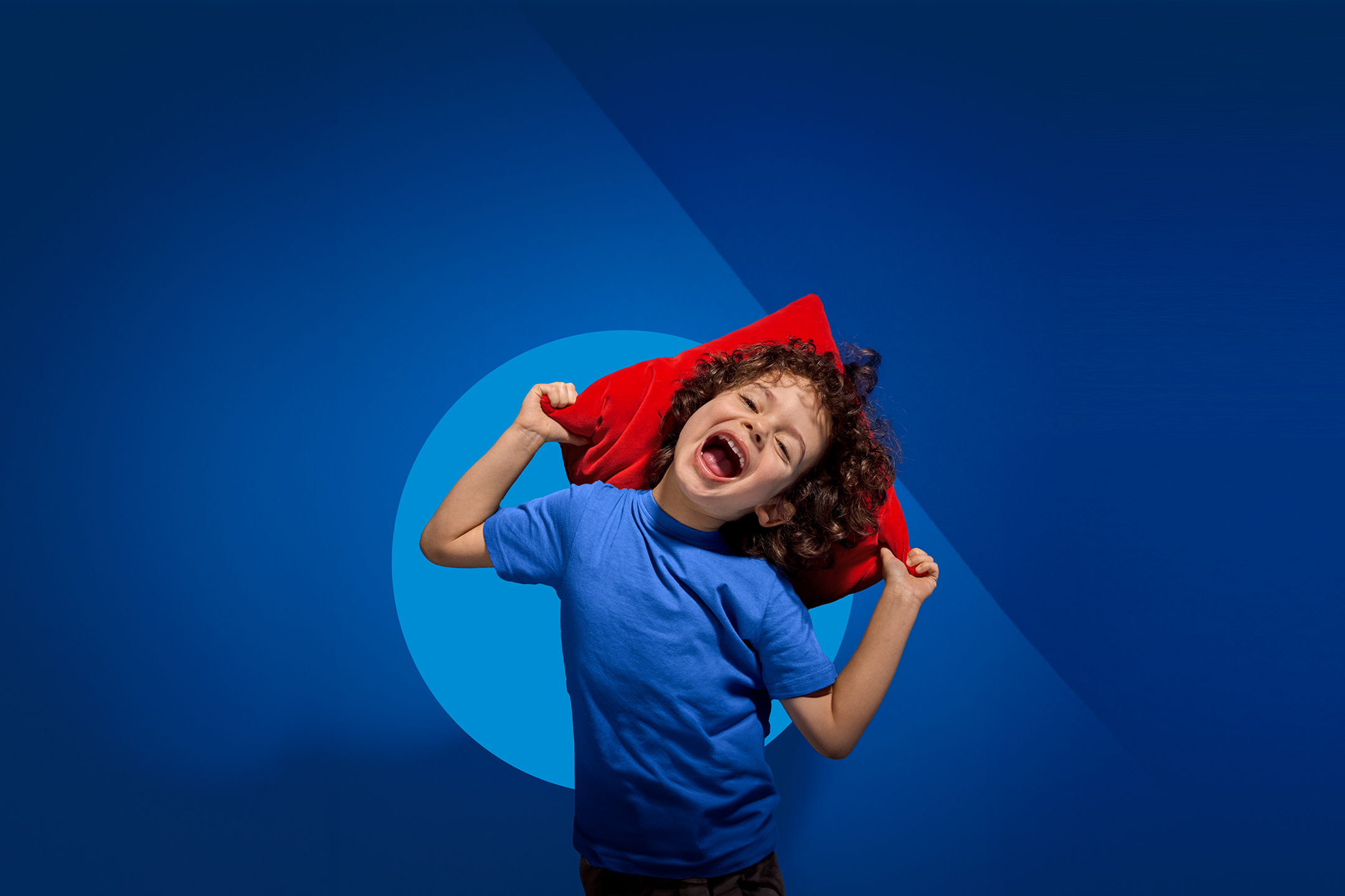 Sretno dijete s plavom majicom i crvenim jastukom na plavoj pozadini.