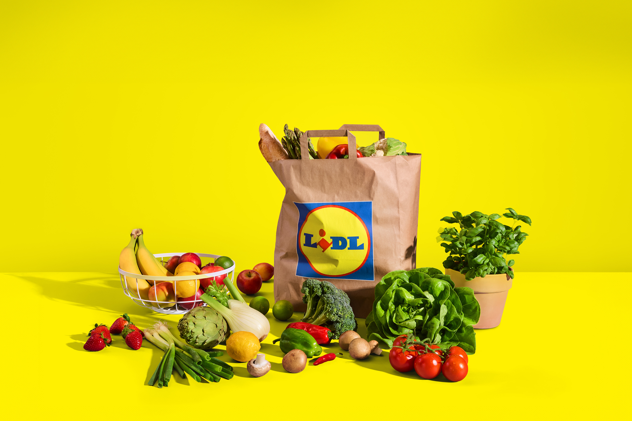Papirnata vrećica s namirnicama i svježim voćem i povrćem na žutoj pozadini.