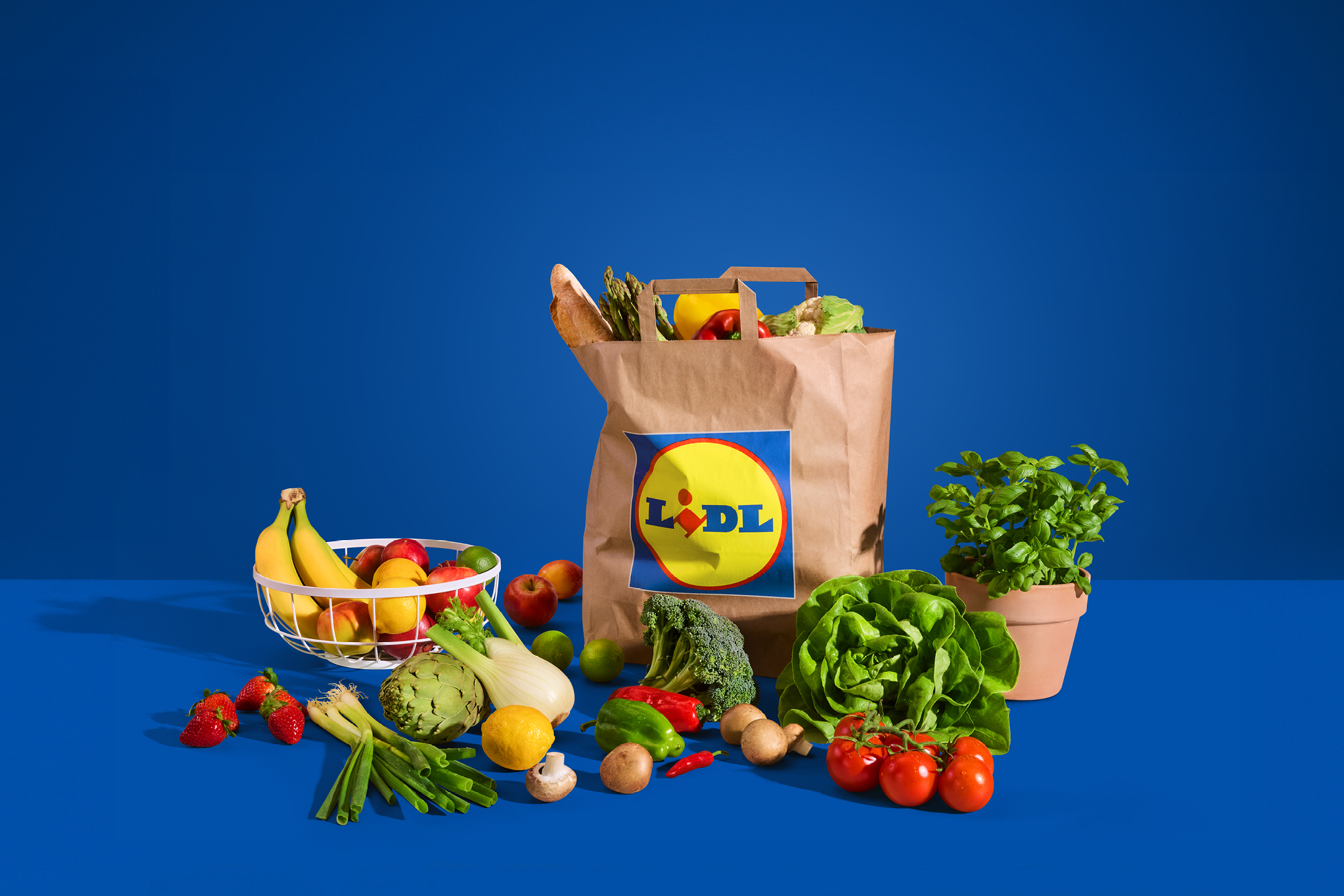 Papirnata vrećica s namirnicama, voćem i povrćem na plavoj pozadini.