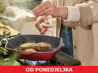 Osoba začinjava odrezak na crvenoj grill tavi na plinskom štednjaku.