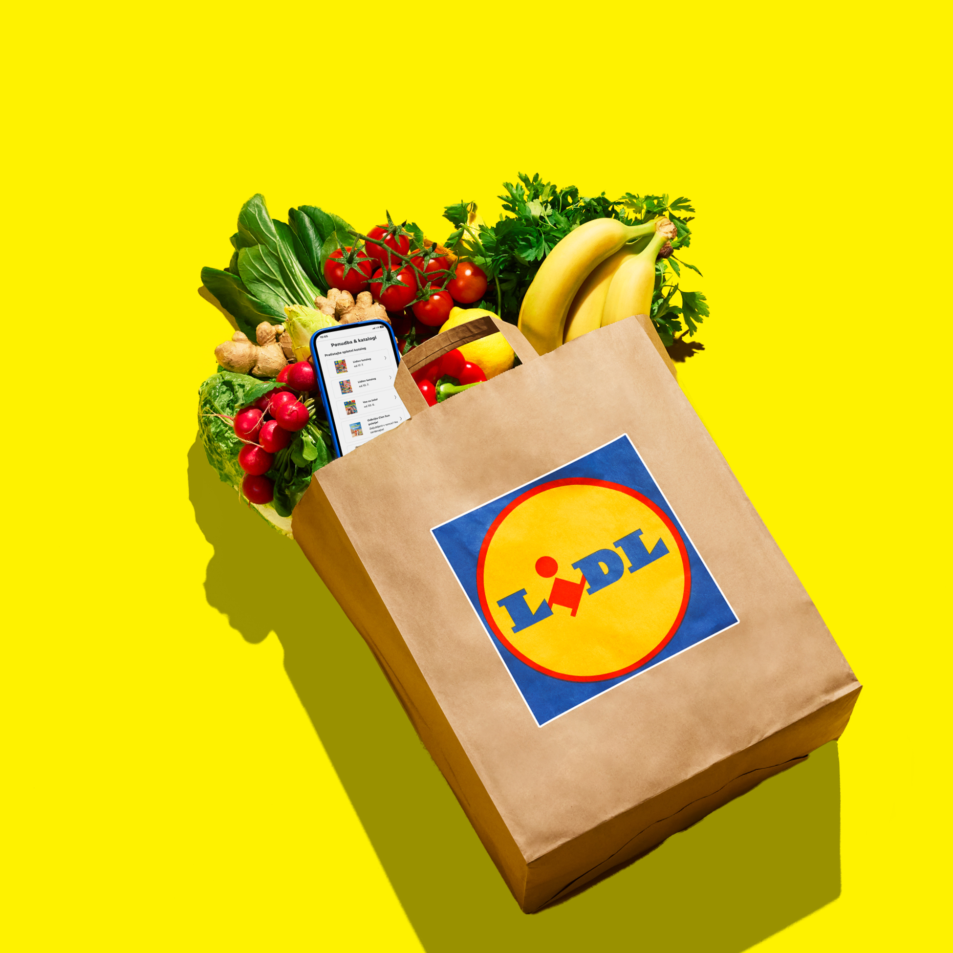 Papirnata vrećica puna svježeg voća i povrća, s telefonom koji prikazuje aplikaciju za kupovinu.