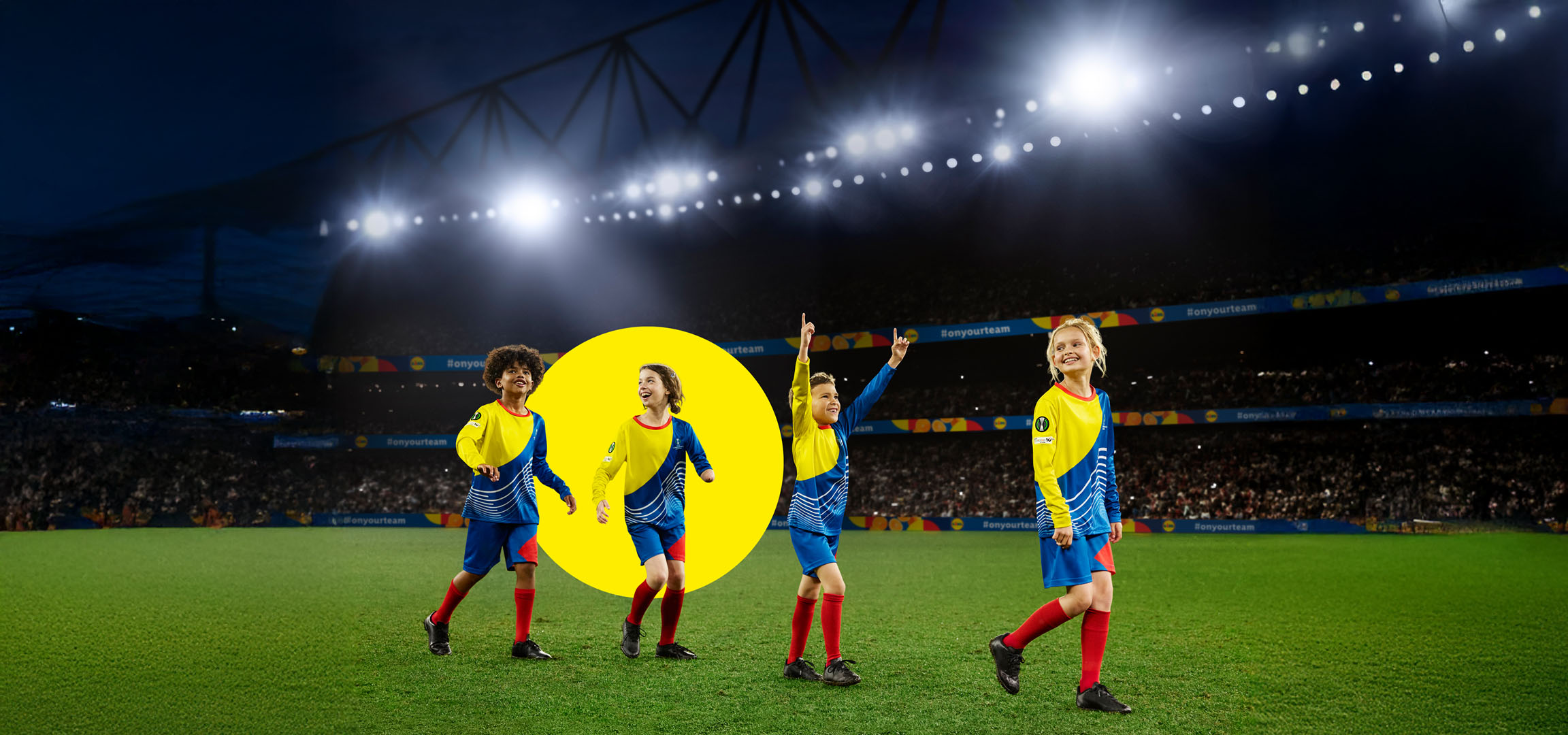 Djeca u nogometnim dresovima na terenu pod svjetlima stadiona.