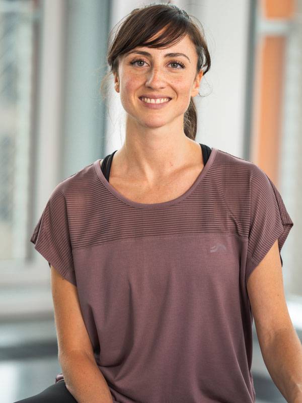 Nasmijana žena u ljubičastom sportskom topu kratkih rukava.