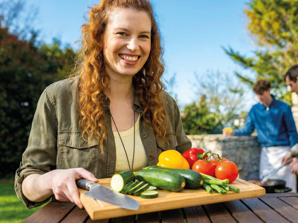 Žena drži dasku za rezanje sa svježim povrćem poput tikvica, rajčica i paprika, spremnih za roštilj.