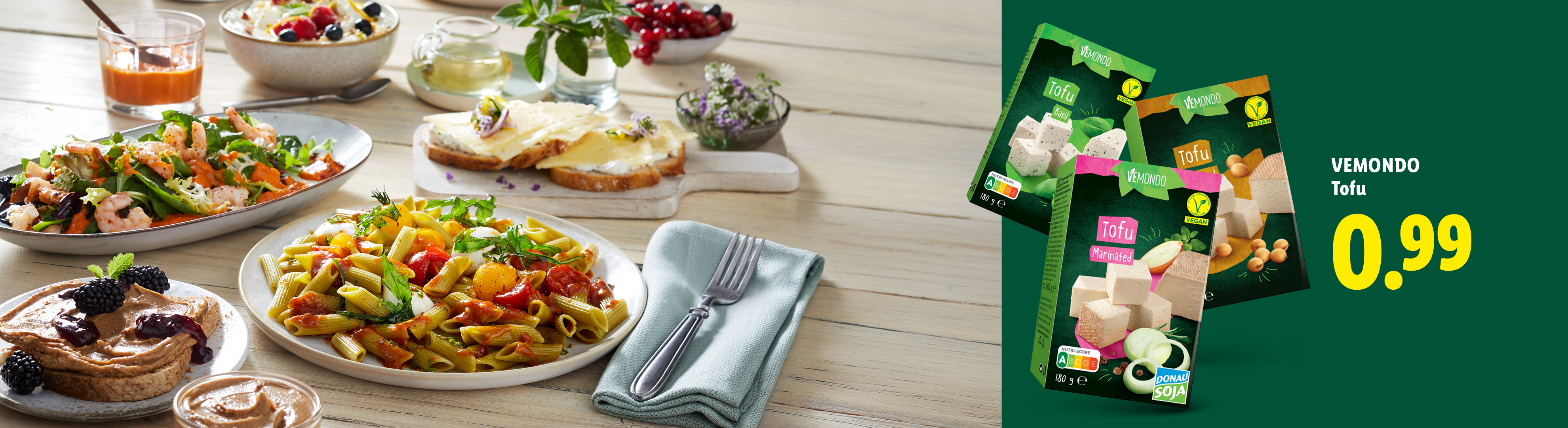 Raznovrsna jela na stolu, uključujući salatu, tjesteninu i tost, s pakiranjima tofua u pozadini.