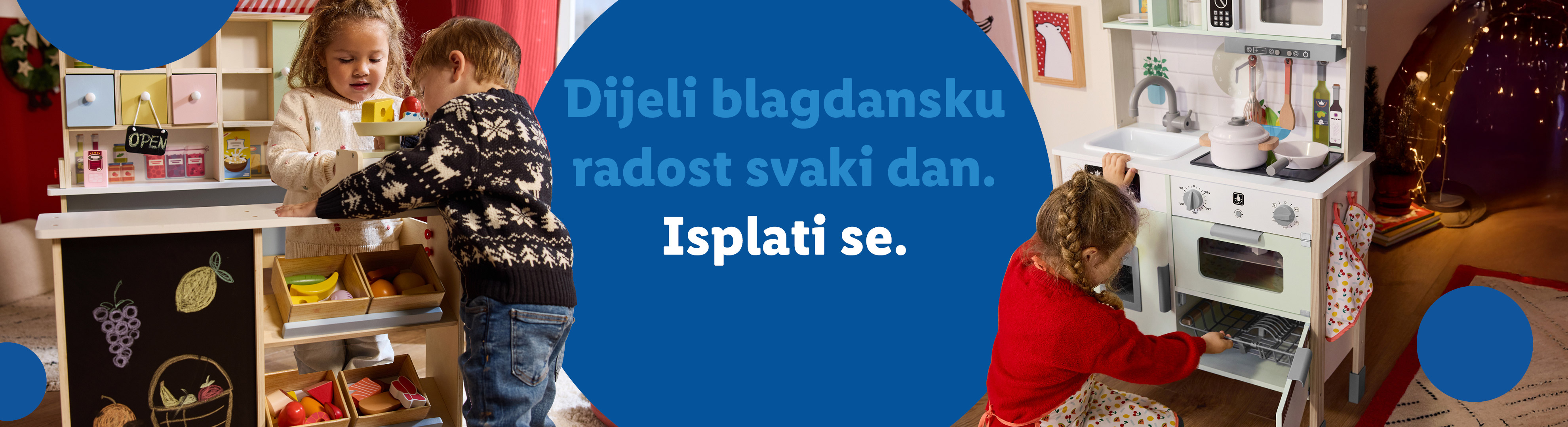 Dvoje djece igra se s drvenom kuhinjom i štandom s hranom, s tekstom: 'Dijeli blagdansku radost svaki dan. Isplati se.'