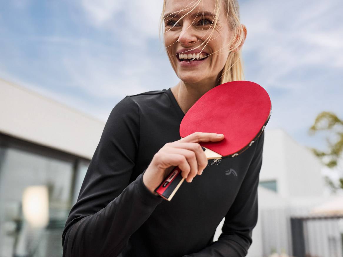 Žena se smiješi držeći reket za stolni tenis.