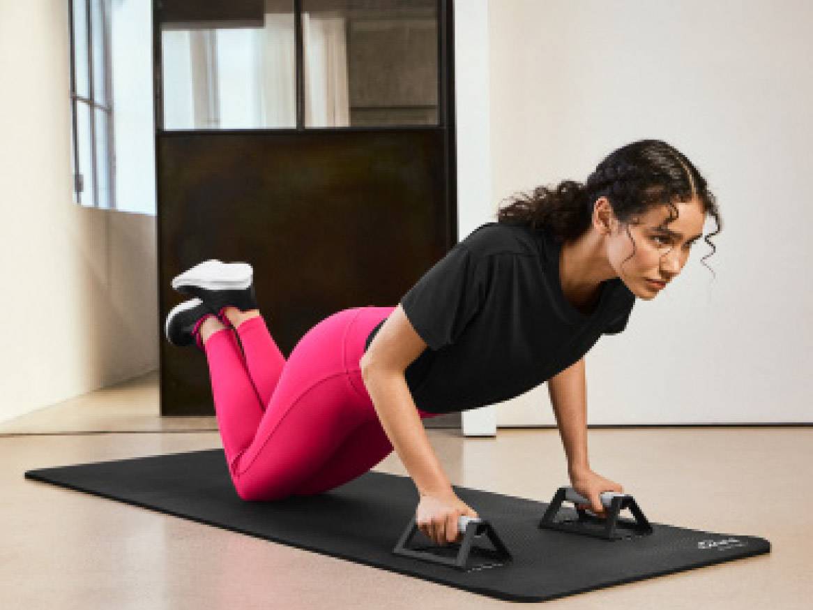Žena u sportskoj odjeći izvodi vježbu s push-up držačima na podlozi za vježbanje.