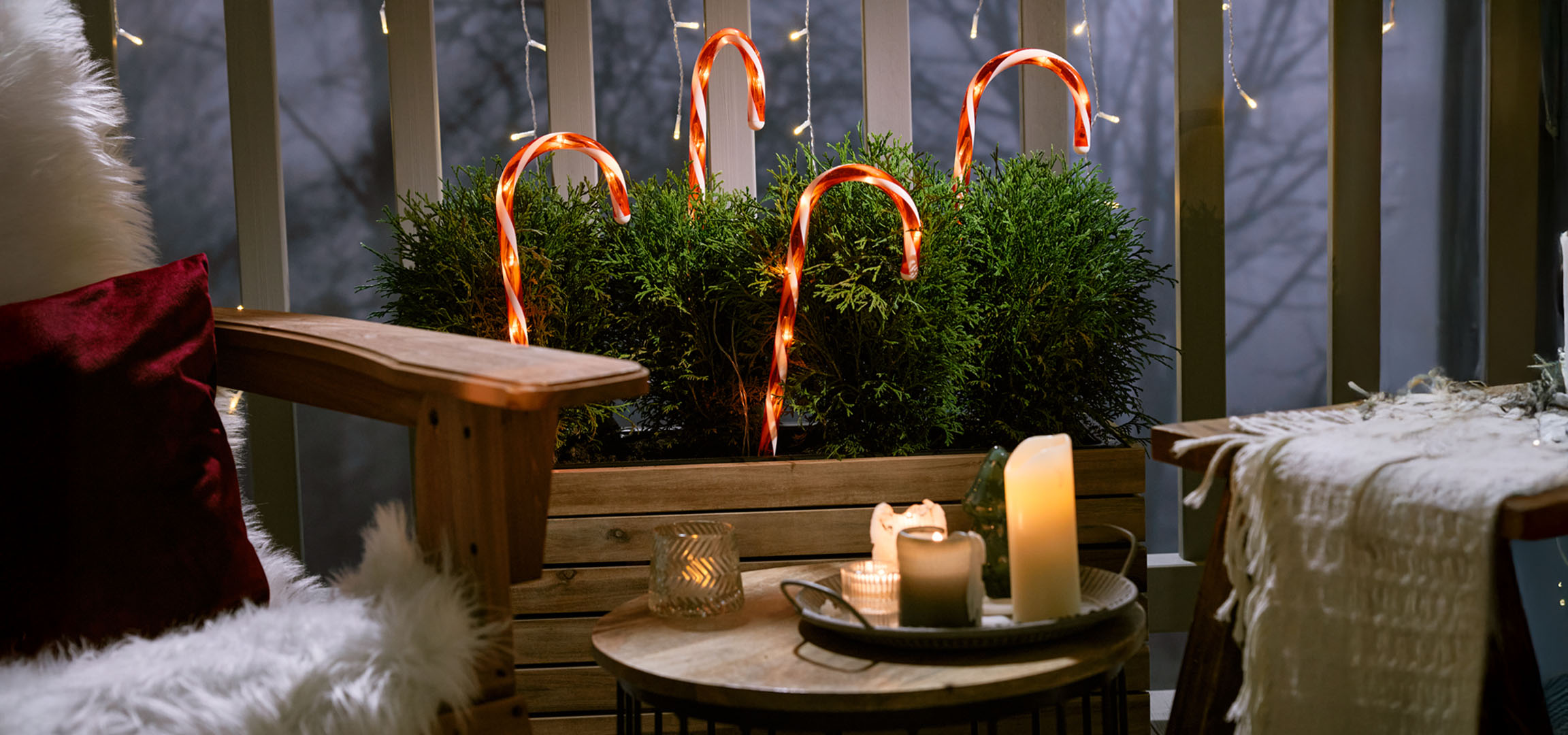 Božićno uređen balkon sa stolicom, svijećama i bombonima u obliku štapa.