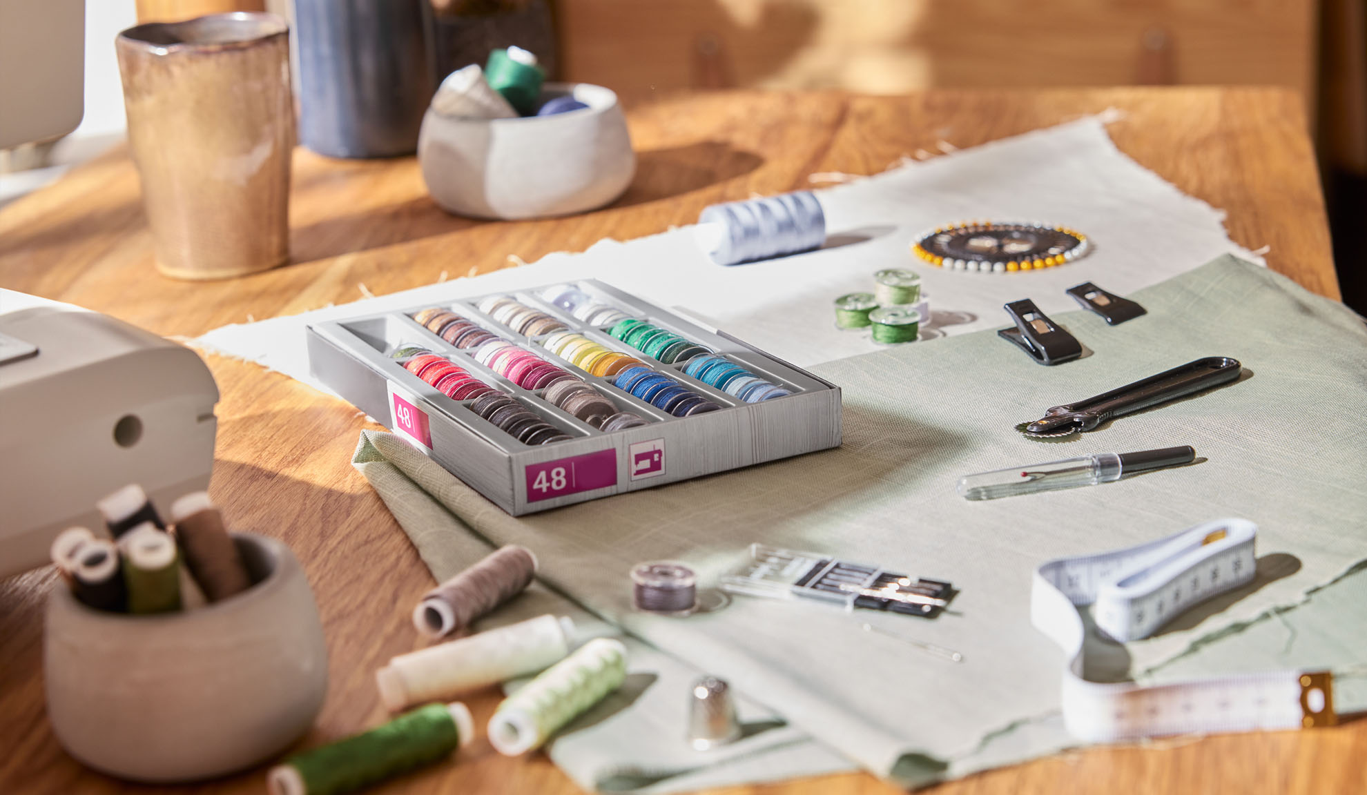 Set za šivanje s kutijom šarenih konaca, šivaćim strojem i raznim alatima na drvenom stolu.