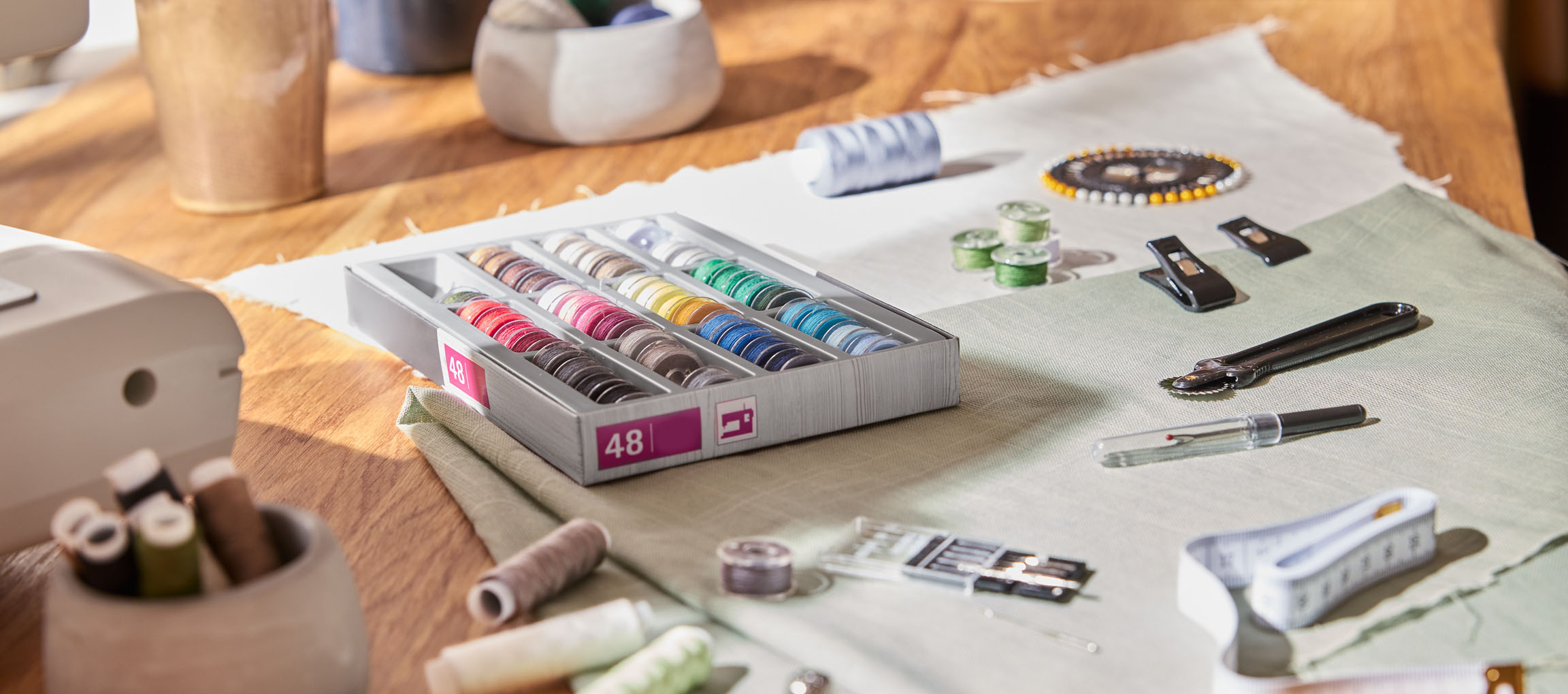 Pribor za šivanje na drvenom stolu, uključujući organizator konca s 48 kalemova, tkaninu i razne alate.