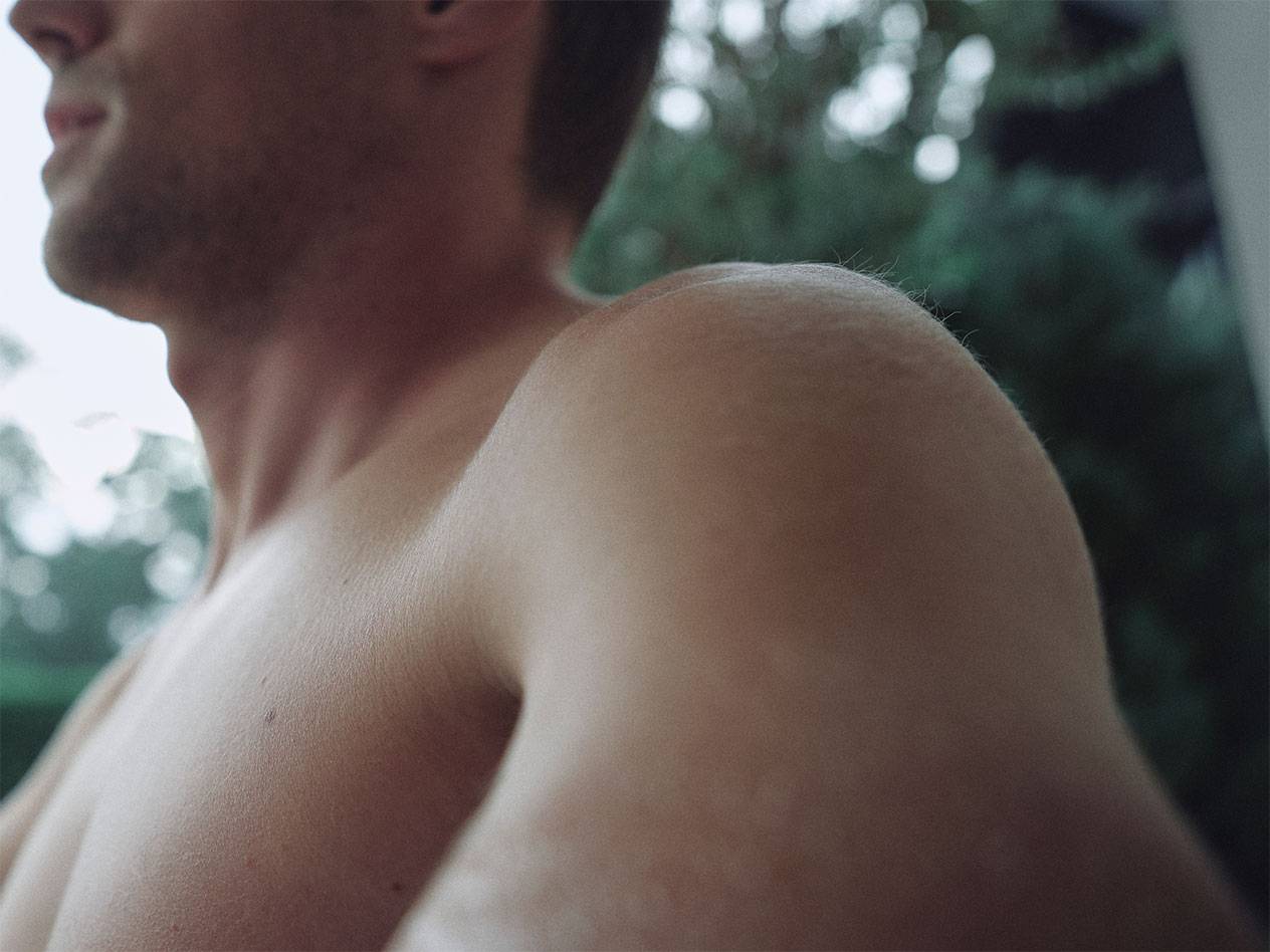 Krupni plan muškog ramena i vrata, s mutnom zelenom pozadinom.