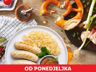 Tanjur s kobasicama i kiselim kupusom, pereci i sirovo meso na drvenoj dasci.