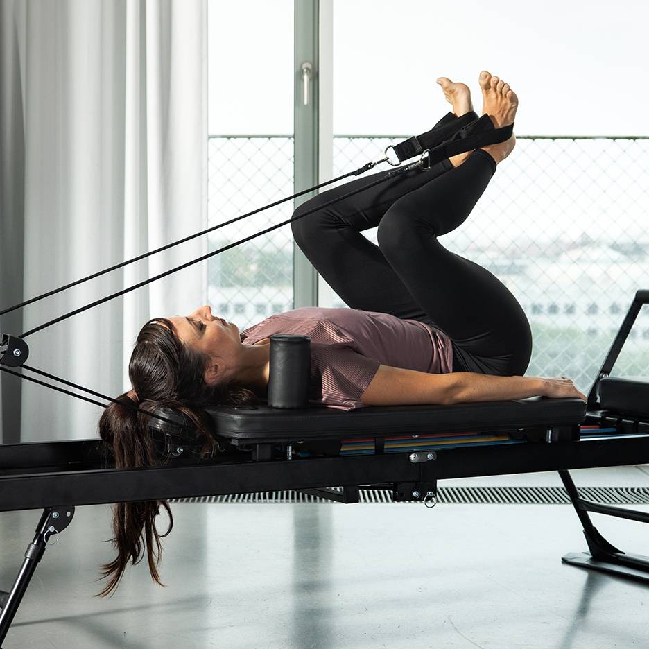 Žena vježba noge na Pilates reformer spravi s trakama otpora.