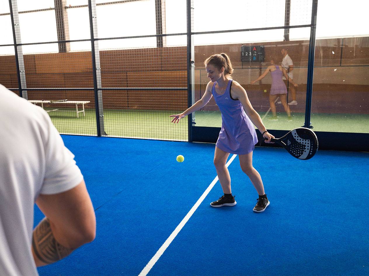Žena u ljubičastoj sportskoj haljini igra padel s reketom i lopticom.