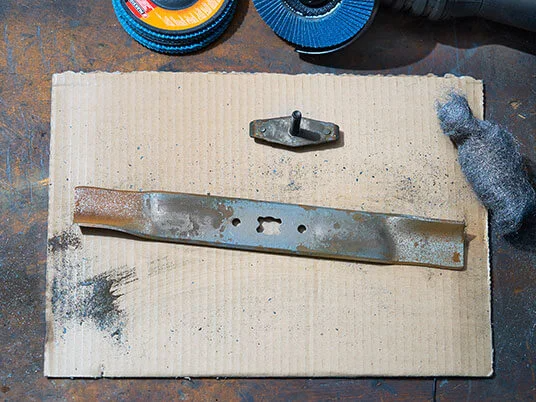 Zahrđala oštrica kosilice na kartonu s abrazivnim diskovima i čeličnom vunom.