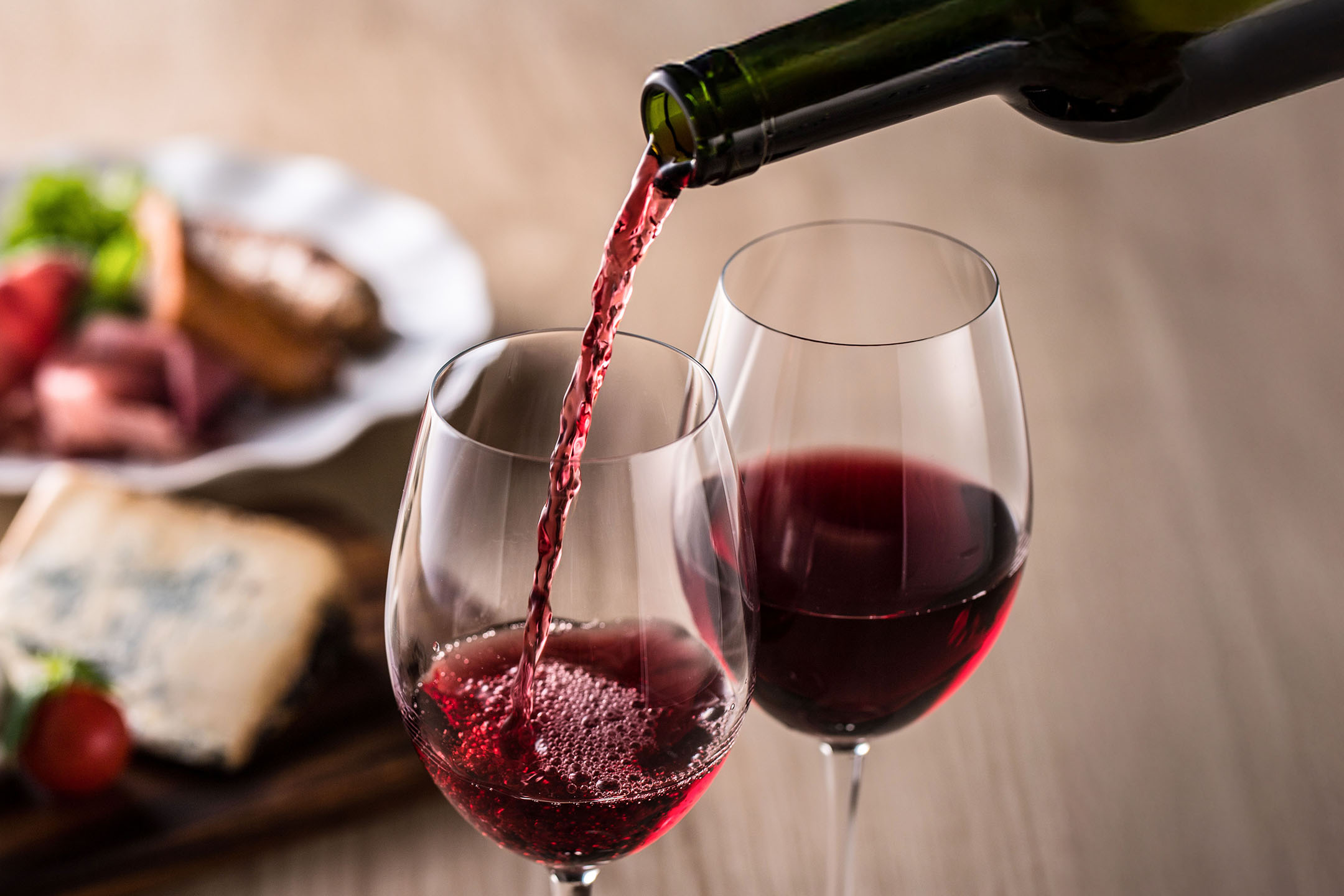 Crno vino se toči u čašu, s predjelima u pozadini.