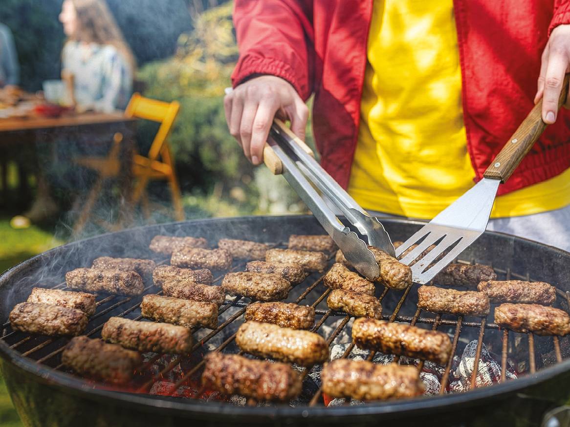 Osoba peče ćevape na roštilju u vrtu.