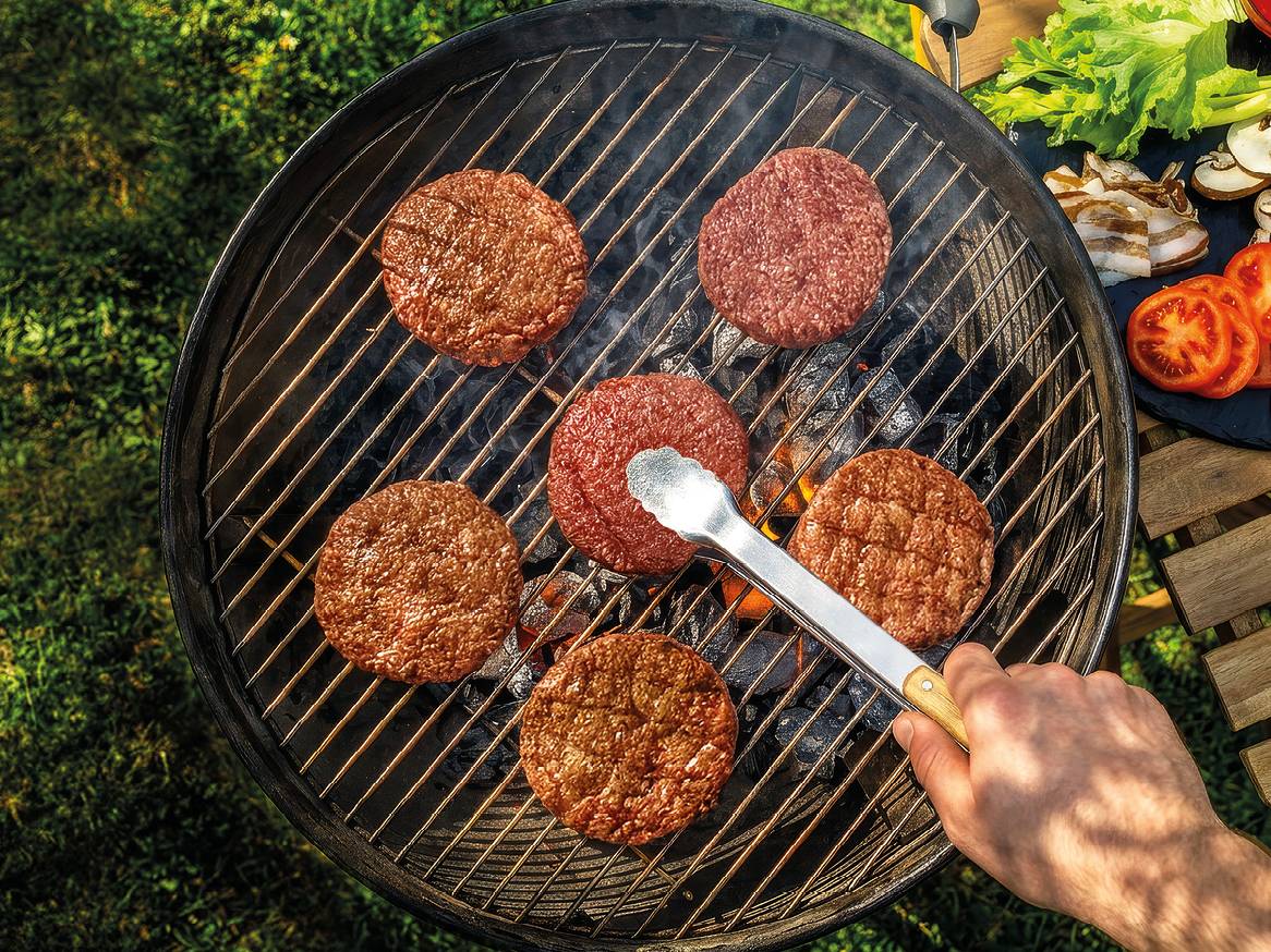 Pljeskavice na roštilju s ugljenom, s rukom koja okreće jednu pljeskavicu hvataljkama.