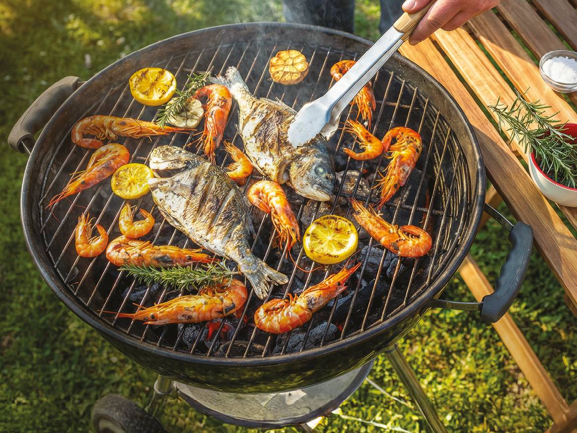 Riba i škampi na roštilju s limunom i začinskim biljem, s rukom koja okreće ribu.