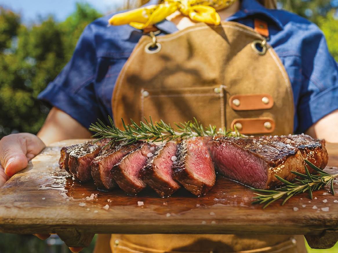 Osoba u pregači drži drvenu dasku s narezanim odreskom, ružmarinom i krupnom soli.