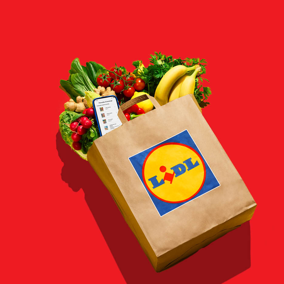 Papirnata vrećica s namirnicama: banane, rajčice, rotkvice, đumbir, zeleno lisnato povrće i mobitel s popisom za kupovinu.