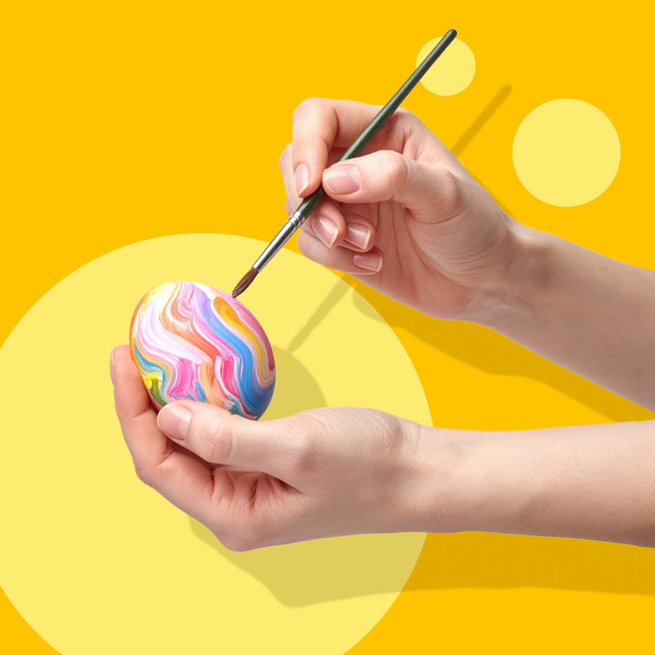 Ruke ukrašavaju šareno jaje kistom, na žutoj pozadini s krugovima.