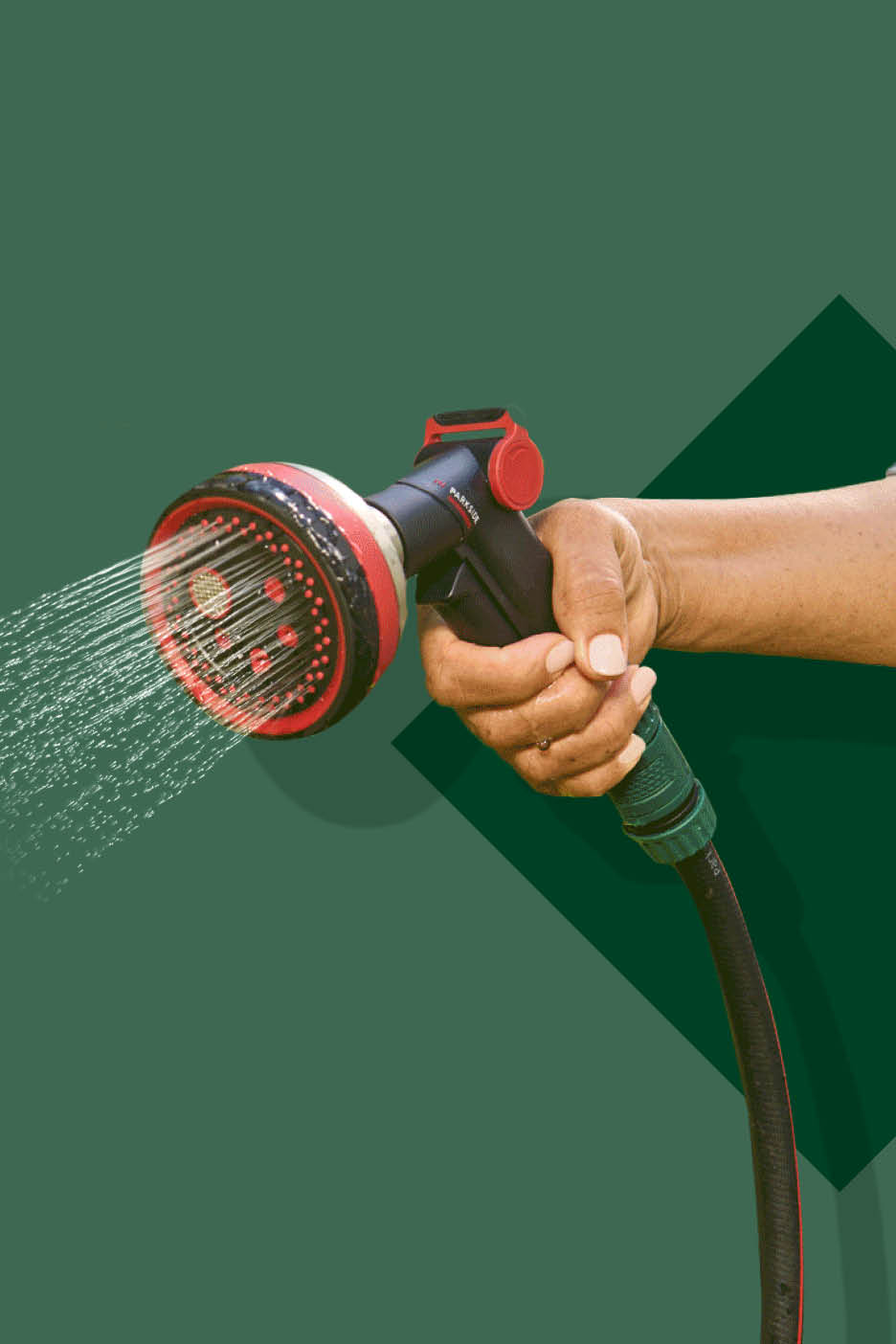 Ruka drži mlaznicu za zalijevanje koja prska vodu, spojenu na vrtno crijevo.