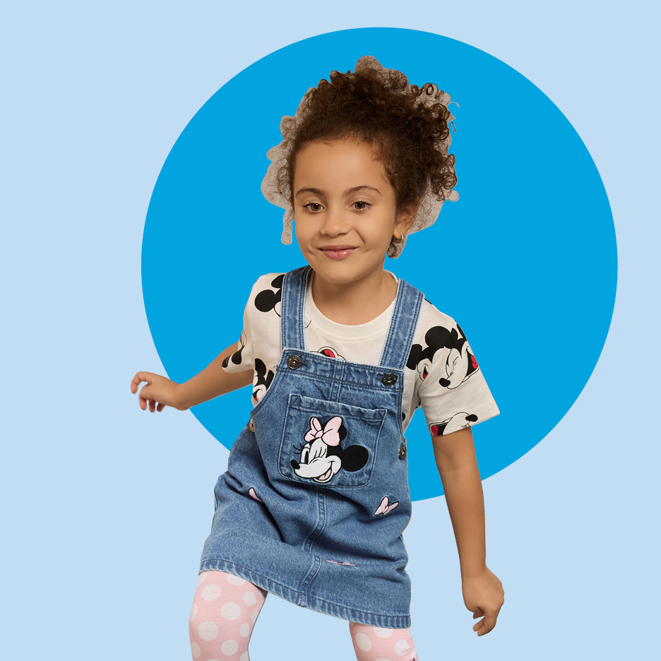 Djevojčica u traper haljini s naramenicama i majici s uzorkom, ružičastim tajicama s točkicama.