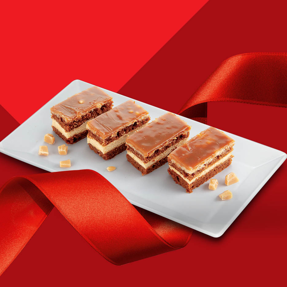 Četiri karamel kocke s kremastim punjenjem na bijelom tanjuru, okružene crvenim vrpcama.