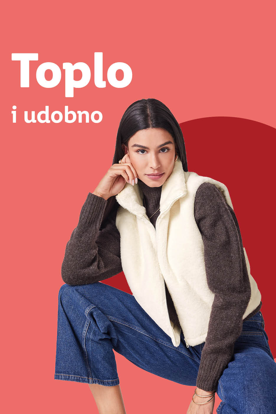 Žena u krem prsluku od flisa, tamnom džemperu i trapericama.