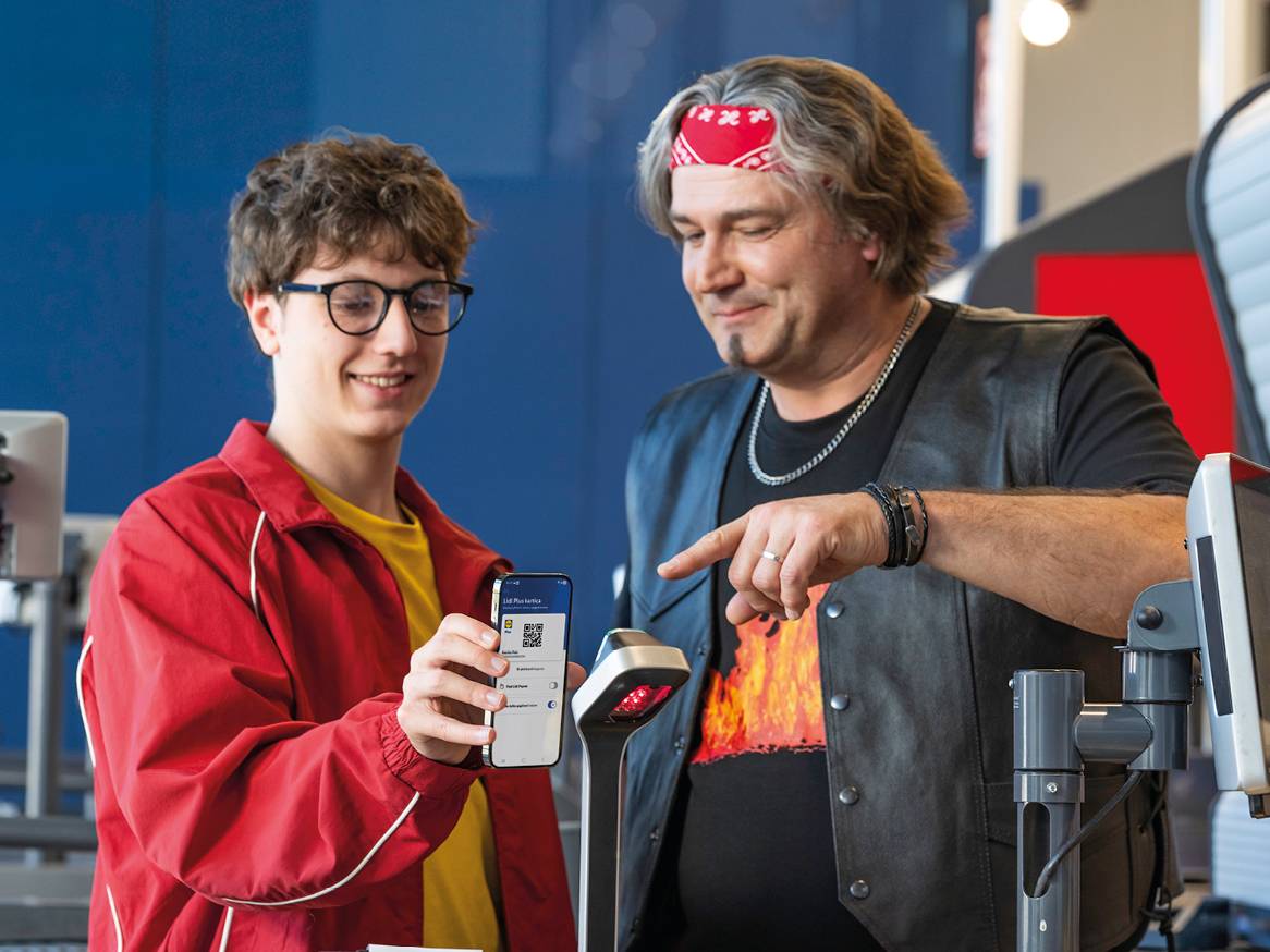 Mladić skenira QR kod s telefona na blagajni, dok stariji muškarac pokazuje.