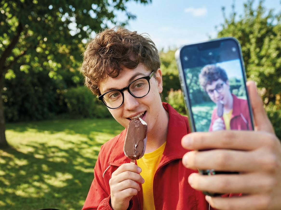 Mladić jede sladoled na štapiću i snima selfie u vrtu.