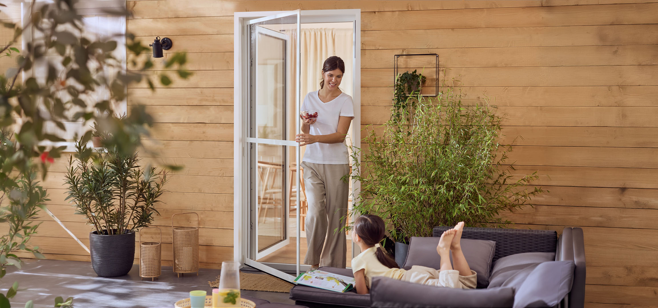 Žena i djevojčica uživaju na terasi s vanjskim namještajem i biljkama.