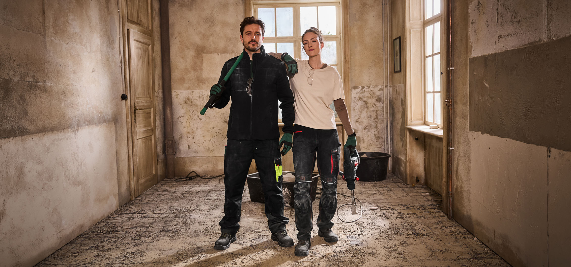 Dva građevinska radnika u radnoj odjeći s alatom na gradilištu.