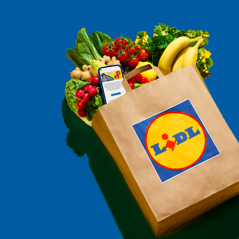 Lidl papirnata vrećica puna svježeg voća i povrća, s telefonom koji prikazuje aplikaciju.