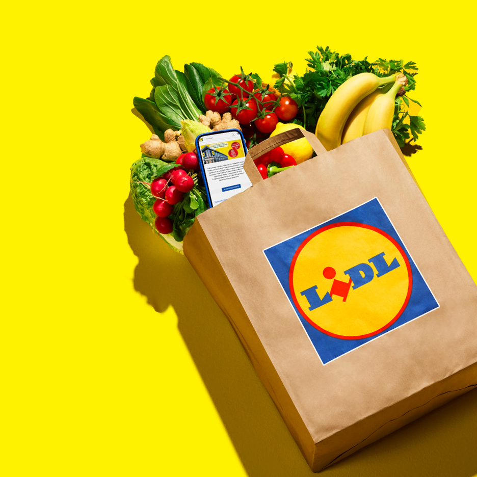 Smeđa papirnata vrećica s logotipom Lidla, puna svježeg voća i povrća, s telefonom unutra.