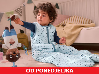 Dijete u plavoj vreći za spavanje s točkicama drži igračku u spavaćoj sobi.