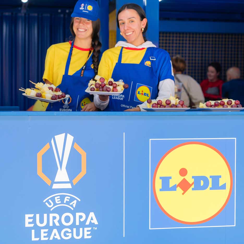 Dvije nasmijane žene u Lidl pregačama nude voće na štapićima na događaju UEFA Europa lige.