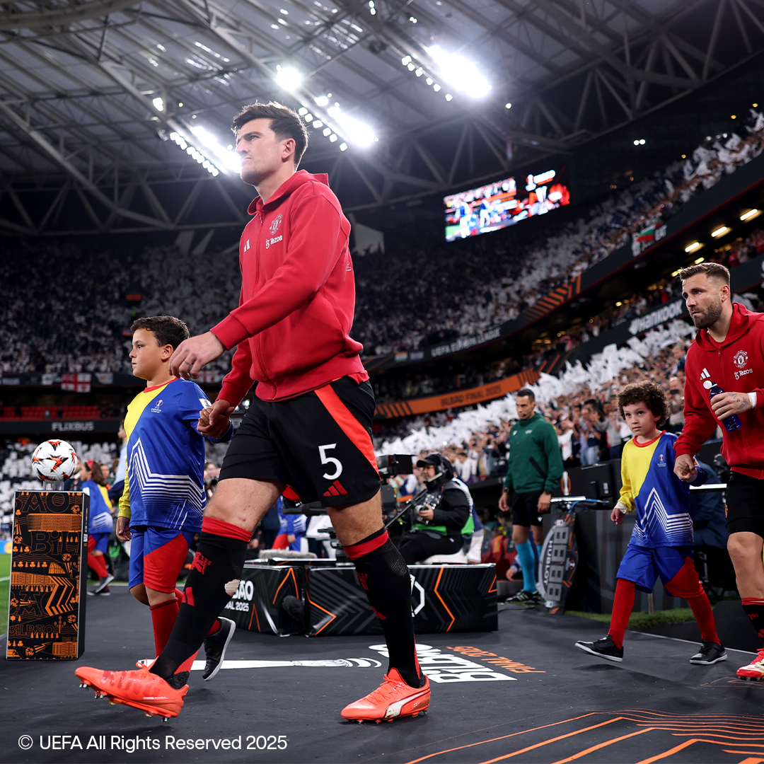 Nogometaši, uključujući jednog s brojem 5, ulaze na teren s djecom na ispunjenom stadionu.