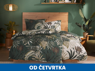 Spavaća soba s drvenim krevetom i posteljinom s tropskim uzorkom, okružena biljkama.