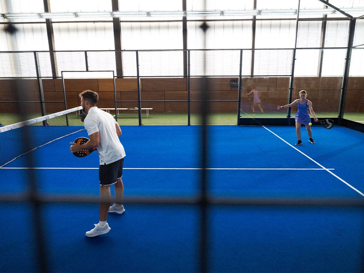 Muškarac i žena igraju padel na plavom terenu s reketima i lopticom.