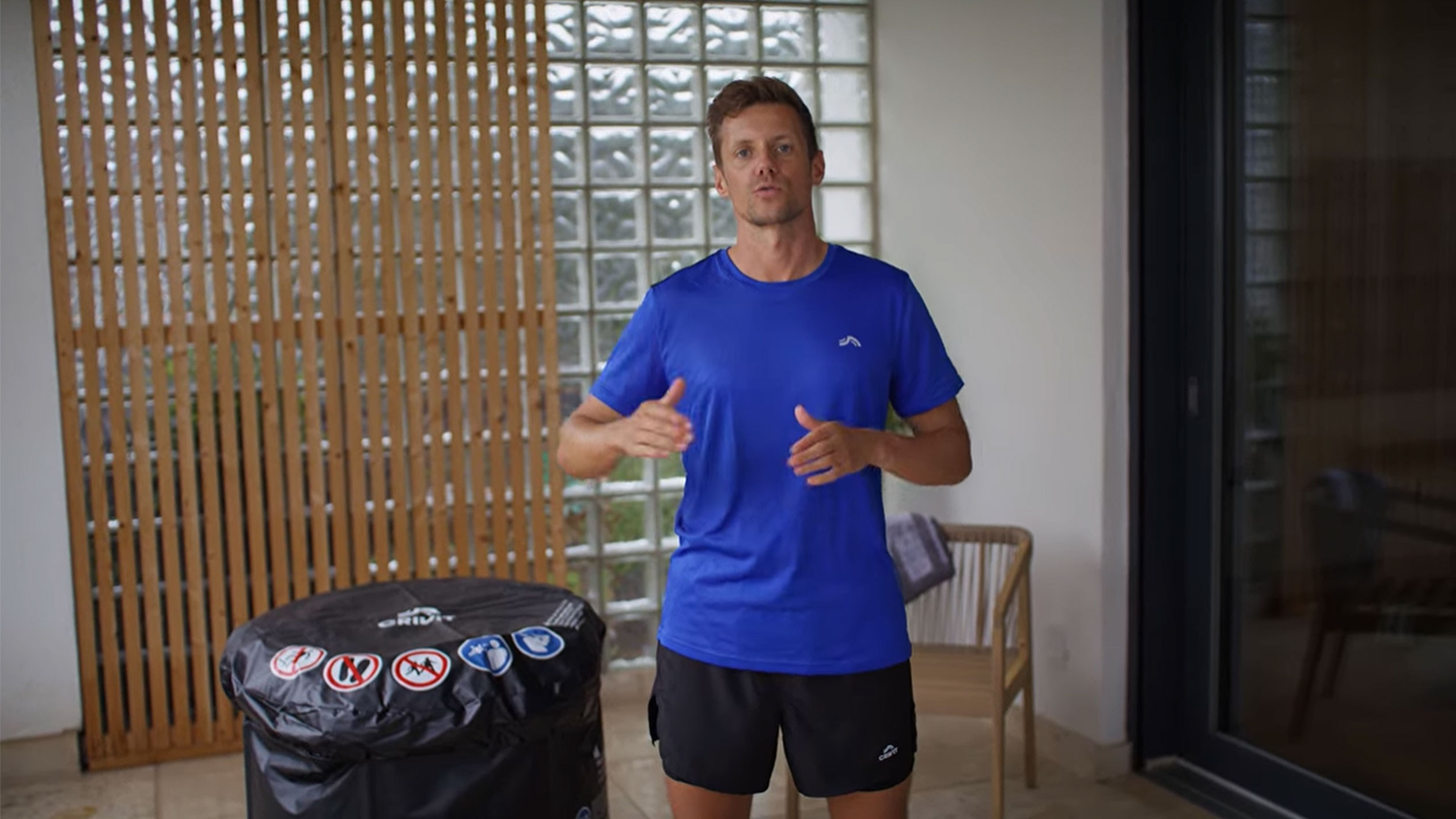 Muškarac u plavoj majici i crnim kratkim hlačama, pored crnog poklopca za hidromasažnu kadu.